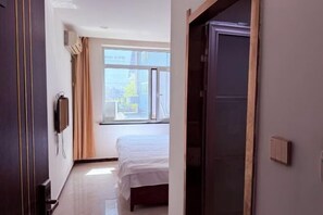 A hotel room with a bed, a TV, a window with curtains, and a door. - Kingdom Hotel (Panjin)