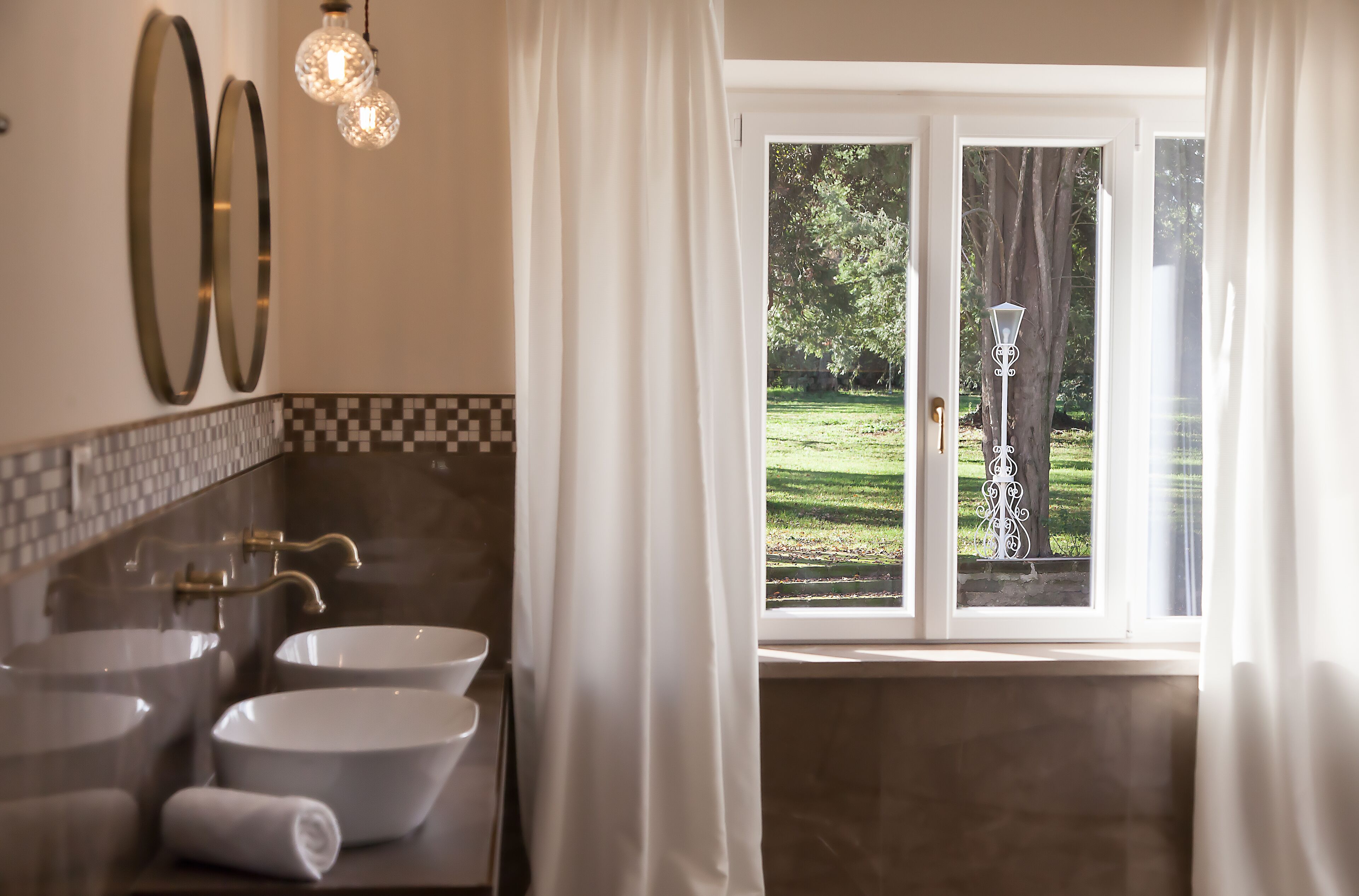 A bathroom with two sinks, a mirror, and a window with curtains.