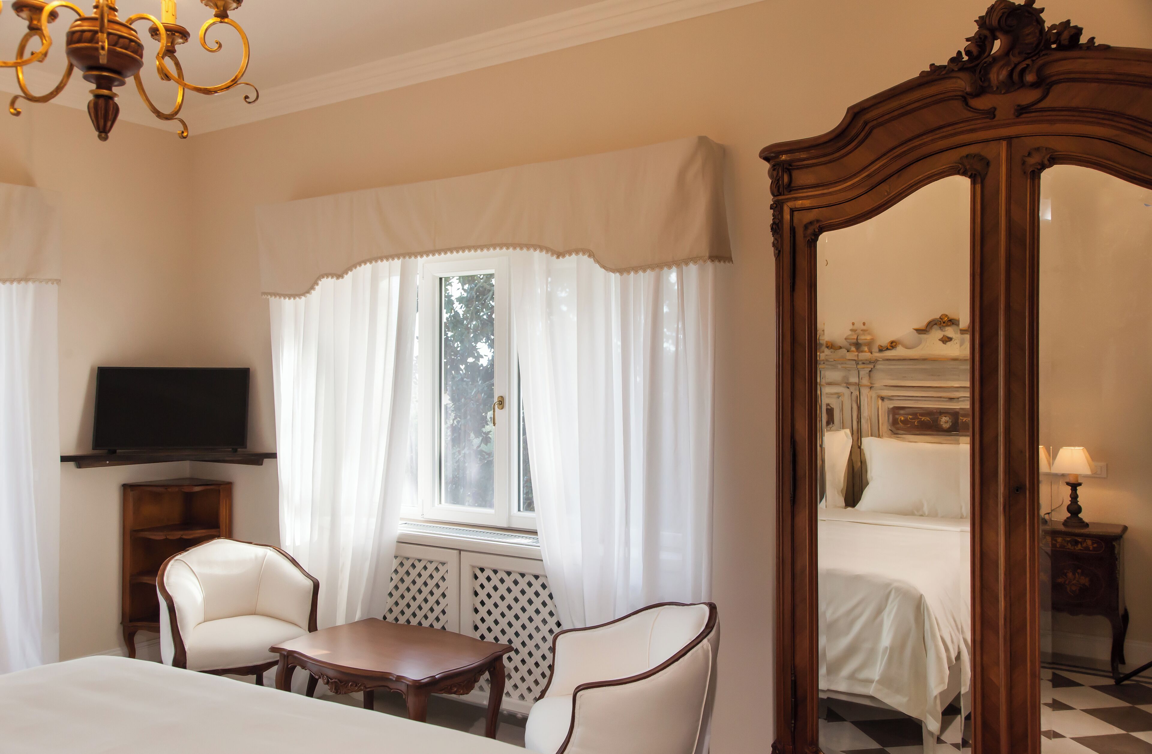 Ein Hotelzimmer mit einem Bett, zwei Stühlen, einem kleinen Tisch, einem Fernseher und einem großen Spiegel.