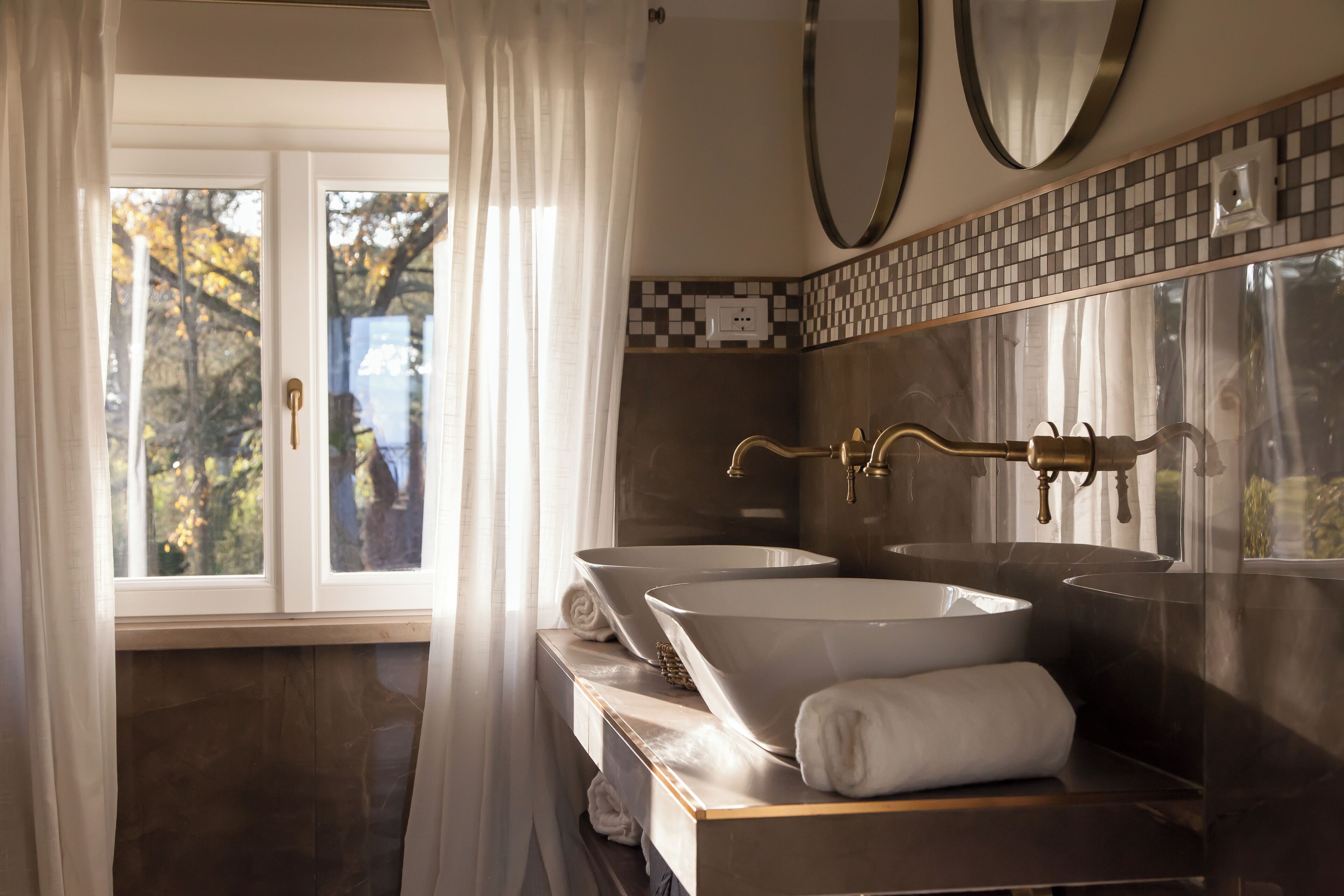 Een badkamer met twee wastafels, een spiegel en een raam met gordijnen.
