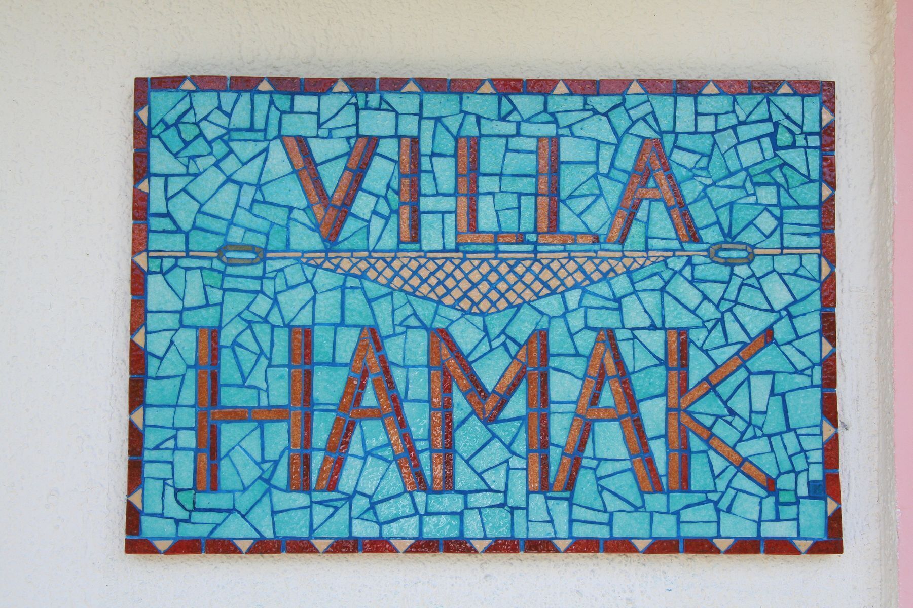 Ein Mosaikschild mit dem Schriftzug 'VILLA HAMAK' an einer Wand.
