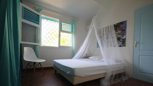 A bedroom with a bed under a canopy, a chair, a window with shutters, and a door.