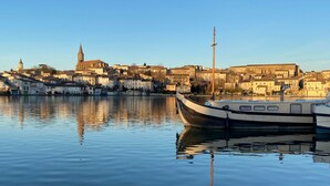 Ein ruhiger Hafen mit einem Boot im Vordergrund und einer historischen Stadt mit Gebäuden und einer Kirche im Hintergrund.