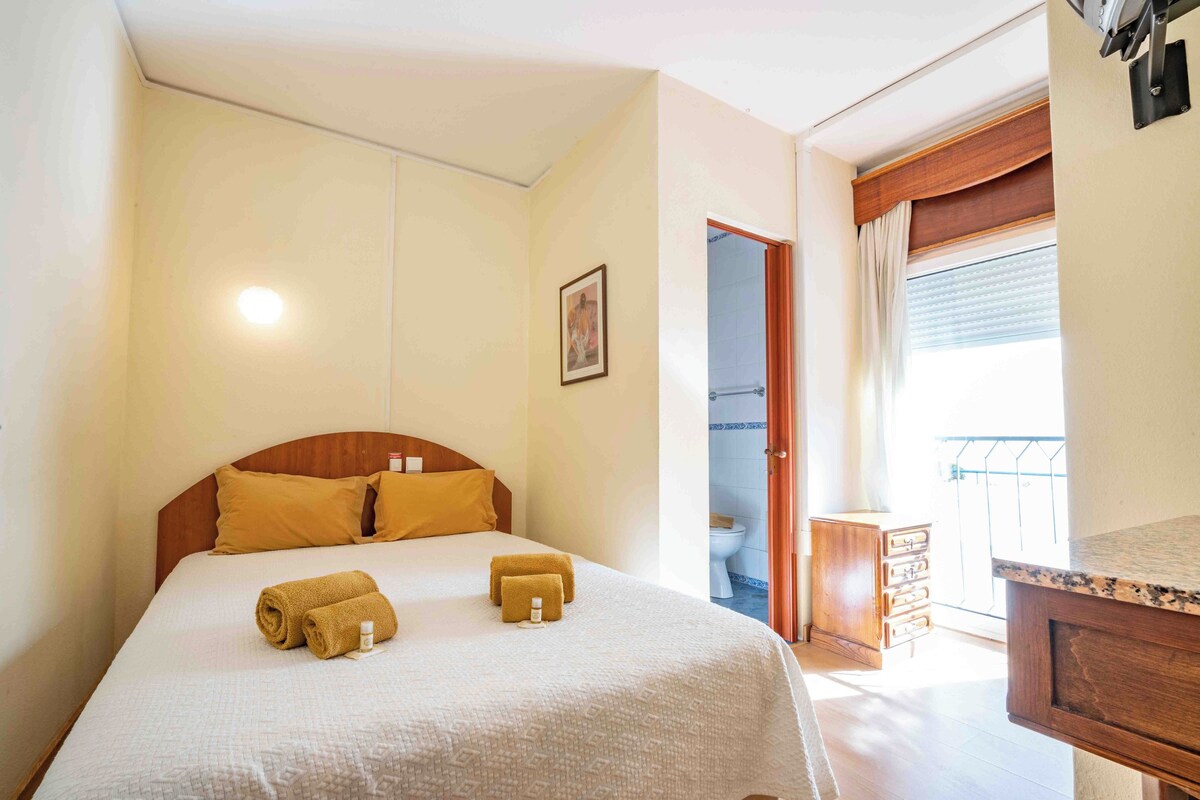A hotel room with a bed, a bedside table, a wooden dresser, and a bathroom visible through an open door.