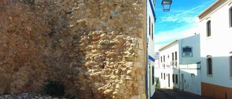 A narrow street with a stone wall on one side and white buildings on the other.