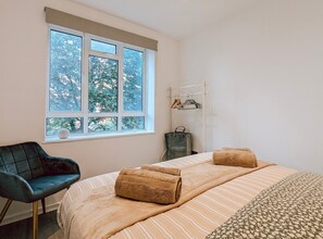 Relax in this serene bedroom with a view of the surrounding trees, featuring a comfortable bed and stylish seating area.