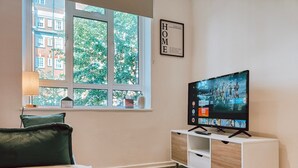 Ein modernes Wohnzimmer mit großem Fenster, Fernseher, Sofa und Schrank.