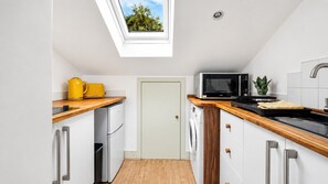 A compact kitchen with a skylight, a microwave, a washing machine, and a small refrigerator.
