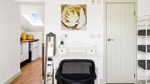Een kamer met een wit bureau, een groot schilderij van een witte bloem, een witte deur en een witte wandplank met opbergdozen.