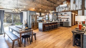 A spacious kitchen with a wooden ceiling, a central island with bar stools, and a dining area with a bench and chairs. - New Rustic Luxe Cabin Billiards Spa Near GSMNP (Townsend)