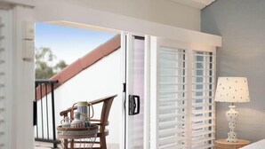 A room with a sliding door leading to an outdoor area, a chair with a basket, and a table with a lamp. - Alice (Bayona 7) - Little Cove (Noosa Heads)