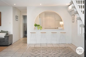 Une cuisine moderne avec des meubles blancs, un îlot central doté de tabourets et un escalier avec des marches en pierre.