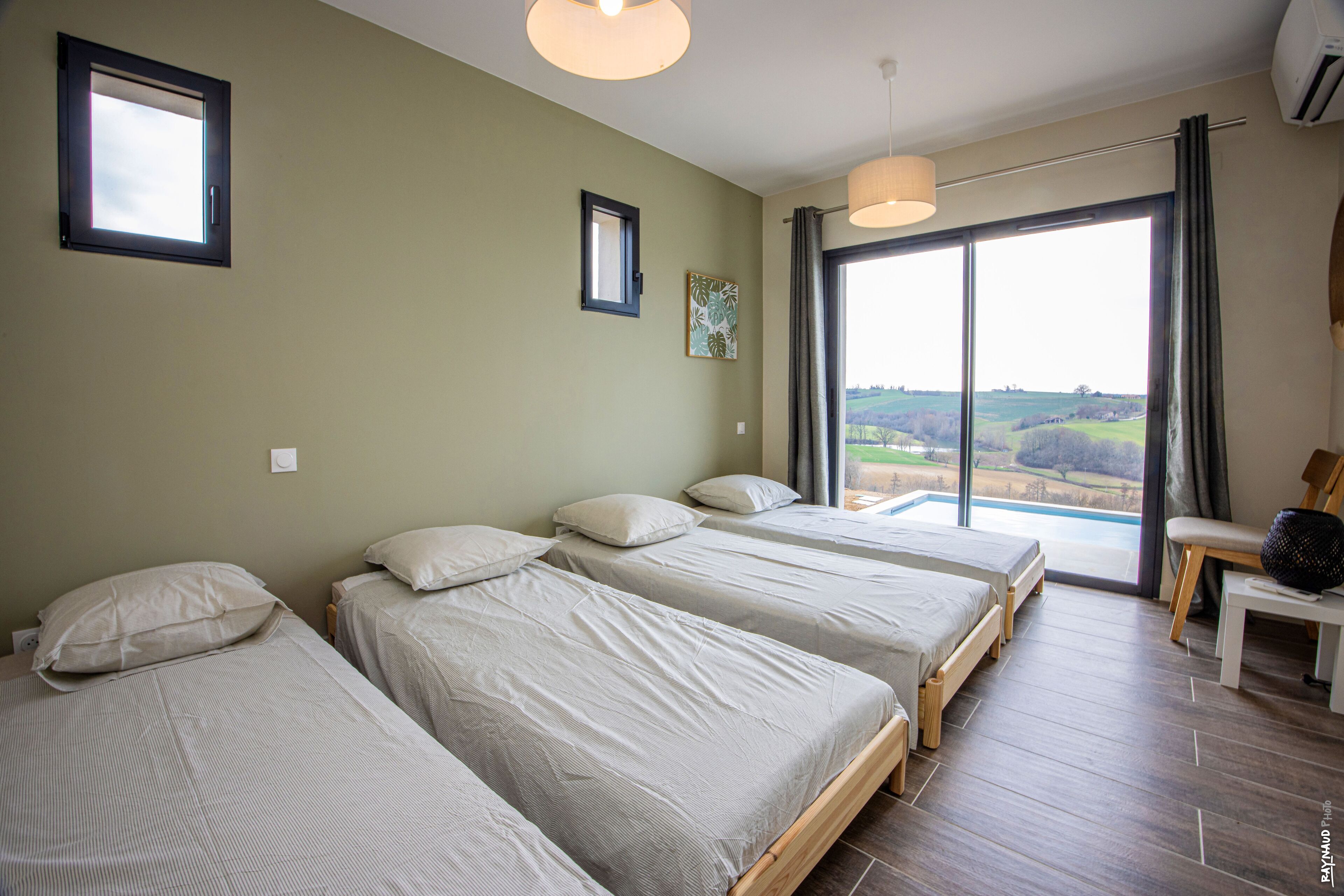 Ein Schlafzimmer mit drei Betten, einem großen Fenster mit Blick und einem Deckenventilator.