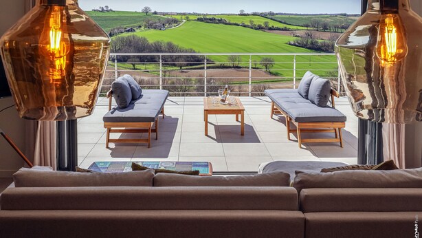 Ein modernes Wohnzimmer mit einem großen Fenster mit Blick auf eine grüne Landschaft. Es gibt zwei Sofas, einen Couchtisch und zwei Pendelleuchten.