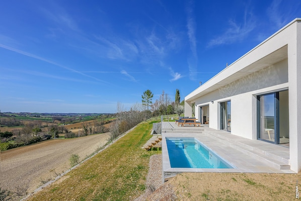 A modern house with a swimming pool, large windows, and a view of the countryside.