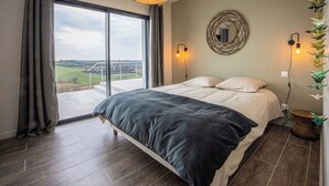 Ein Schlafzimmer mit einem großen Bett, Blick auf die Landschaft und einem runden Spiegel an der Wand.