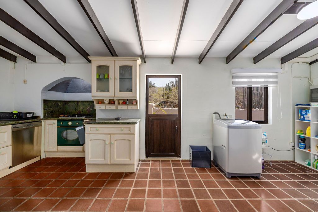 A kitchen with a stove, oven, and refrigerator, a door leading outside, and a window with blinds.