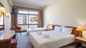 Quarto de hotel com duas camas, uma escrivaninha, uma cadeira e uma televisão.