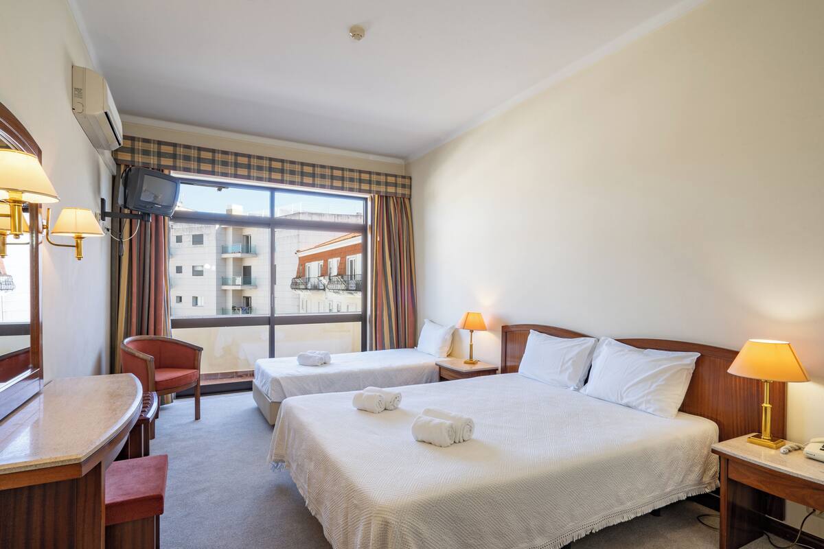 A hotel room with two beds, a desk, a chair, and a TV.