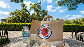 Uma cesta de piquenique com comida, uma garrafa de água, uma xícara e uma bolsa com um logotipo.