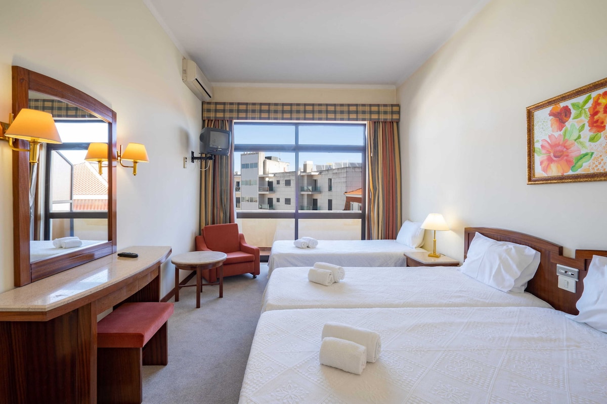 Habitación de hotel con dos camas, un escritorio, una silla, un televisor y una ventana con vistas a la ciudad.