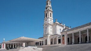 Um edifício histórico com uma alta torre do relógio, uma entrada coberta e uma estátua em frente.