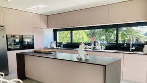 A modern kitchen with a central island, built-in appliances, and a large window providing a view of greenery. - Rent house between sea, town and golf BADEN (Baden)