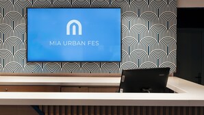 A reception desk with a blue sign reading "MIA URBAN FES" and a patterned wall behind it. - Mia Hotels Fes (Fes)
