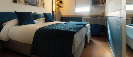 A hotel room with a large bed, a desk, a TV, and a window.