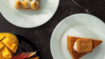 Um prato de sobremesa com um pastel quadrado coberto com merengue, uma fatia de torta com biscoito, e uma tigela de frutas e legumes fatiados.