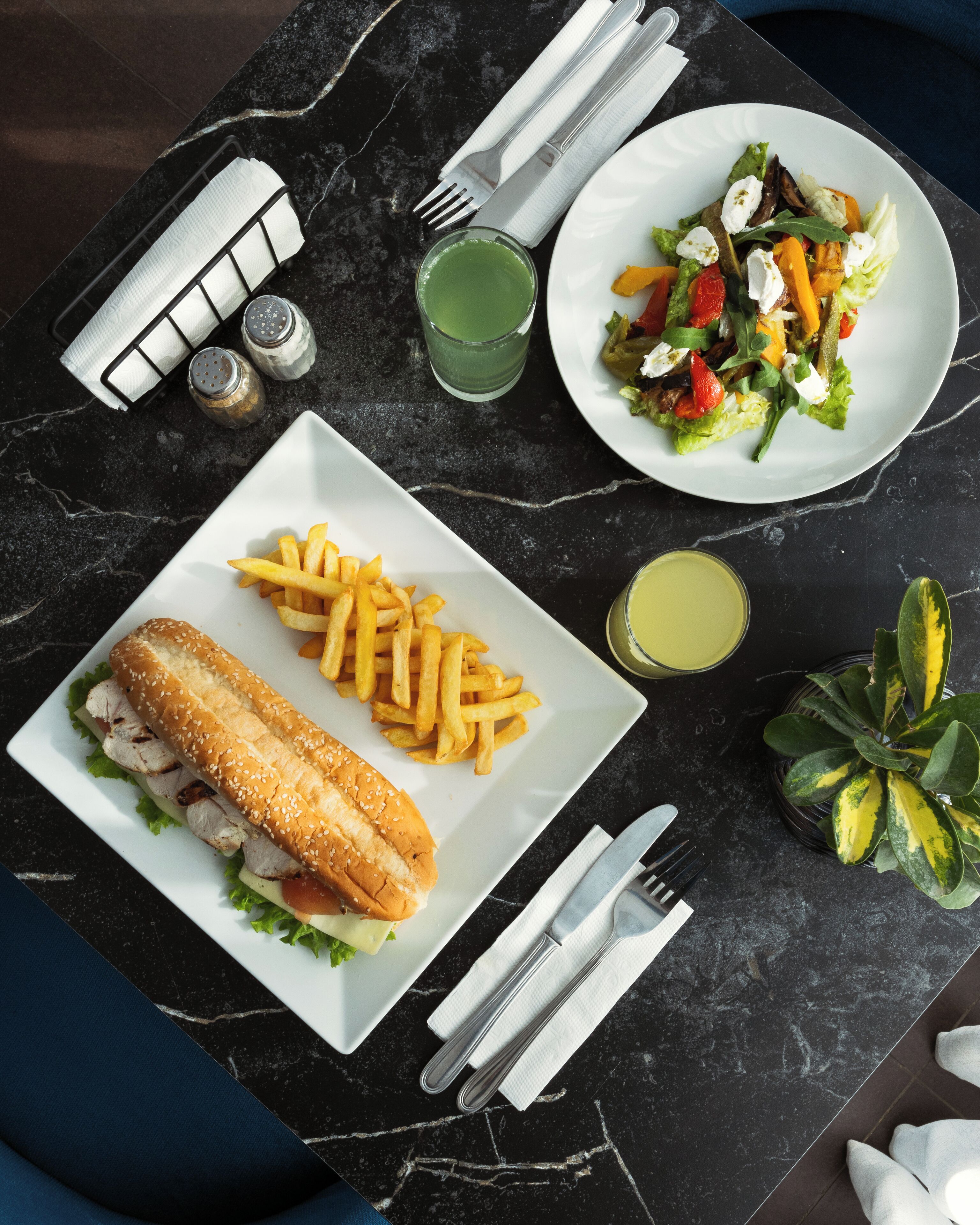 A meal setup with a sandwich, fries, and a salad on a marble table.