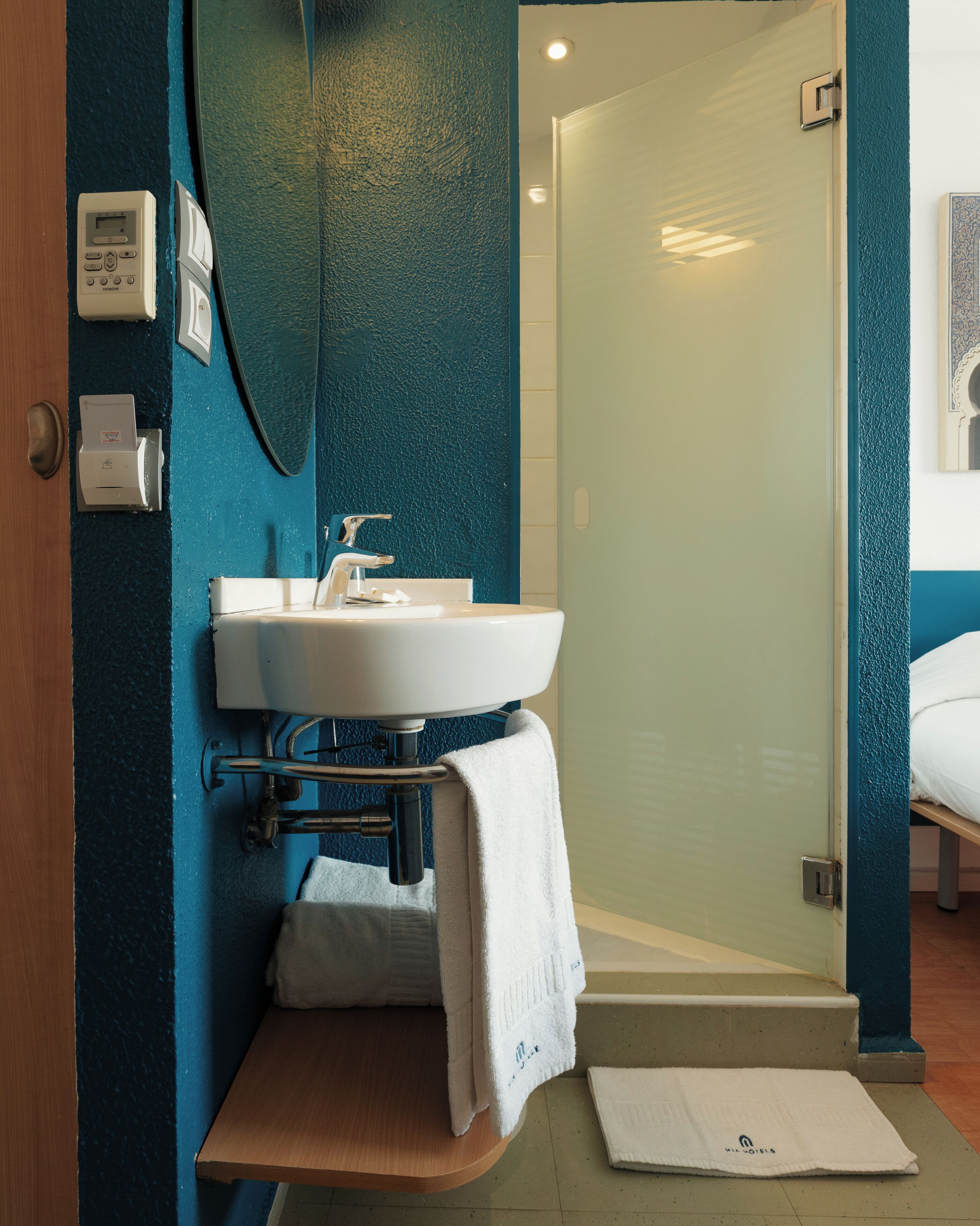 A bathroom with a white sink, a mirror, and a towel on a wooden shelf.