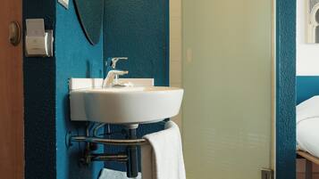 A bathroom with a white sink, a mirror, and a towel on a wooden shelf.
