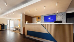 A reception area with a modern design, featuring a wooden reception desk, a clock, and a television displaying the hotel's name. - Mia Hotels Fes (Fes)