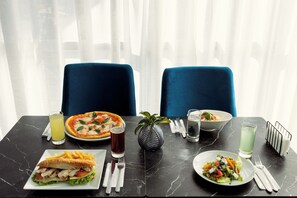 A dining table with a pizza, a sandwich, a salad, and drinks.