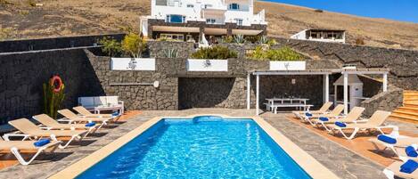 A swimming pool with lounge chairs, a stone wall, and a white building in the background.