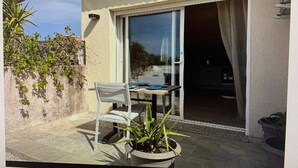 A patio with a table and chairs, a potted plant, and a sliding glass door leading to an interior space. - Apartment 7 minutes from Calvi (Calvi)