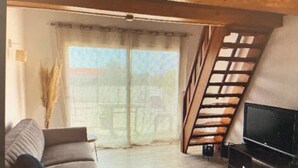 A living room with a sofa, a TV, and a window with curtains. - Apartment 7 minutes from Calvi (Calvi)