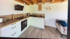 A modern kitchen with a wooden ceiling, a flat-screen TV mounted above the counter, and a built-in oven. - Apartment 7 minutes from Calvi (Calvi)