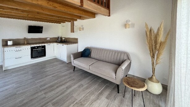 A modern kitchen with a built-in oven, a grey sofa, and a wooden staircase. - Apartment 7 minutes from Calvi (Calvi)
