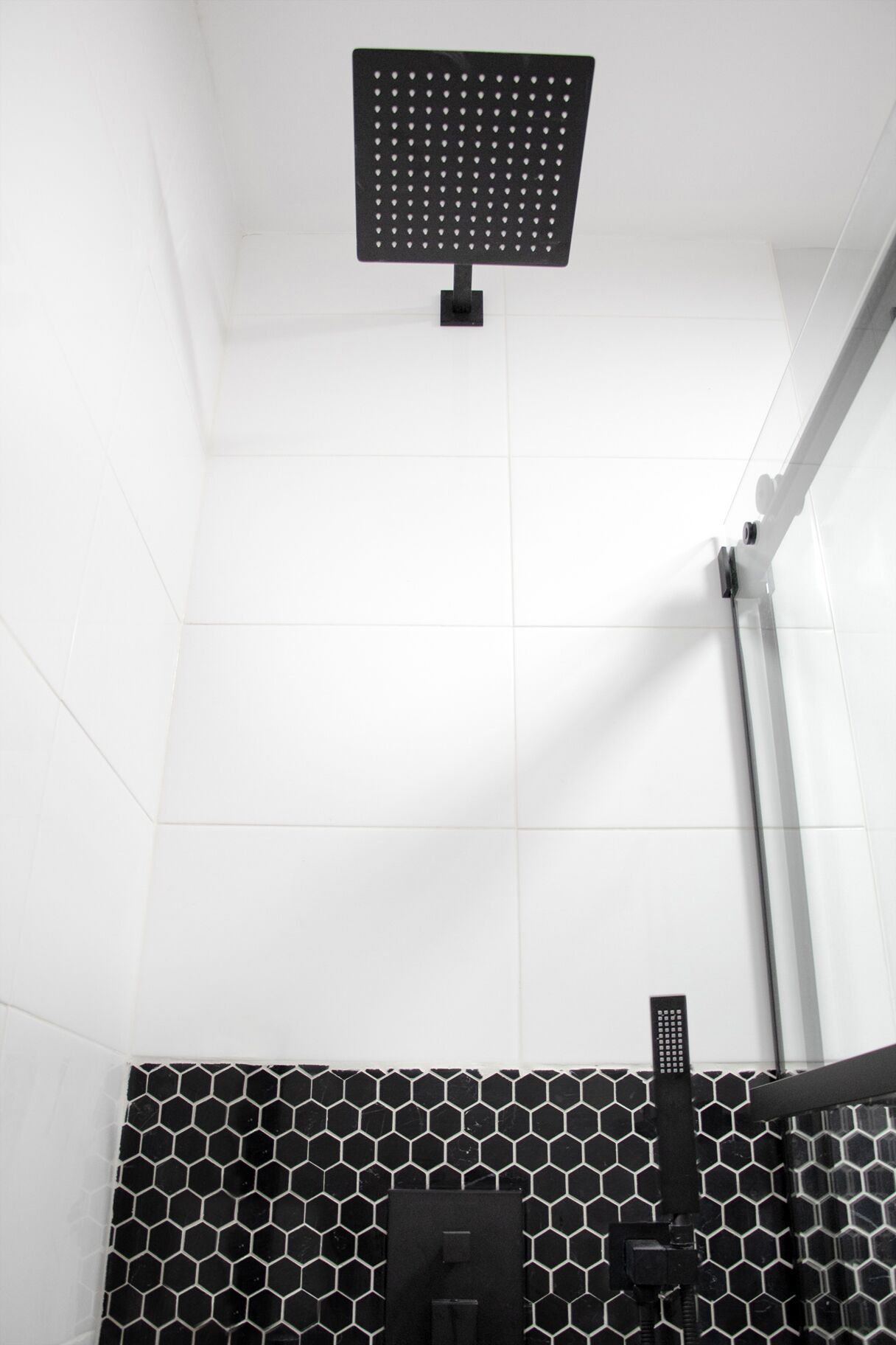 Een douche met een plafonddouche en een zwarte douchekop.
