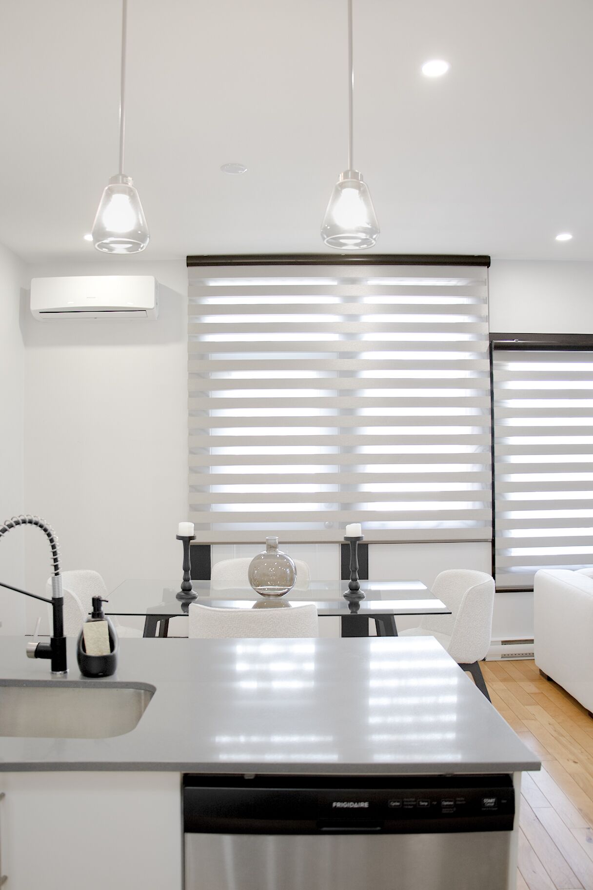 Une cuisine moderne équipée d’un lave-vaisselle, d’un évier et d’un robinet. Deux luminaires suspendus sont fixés au-dessus du plan de travail.
