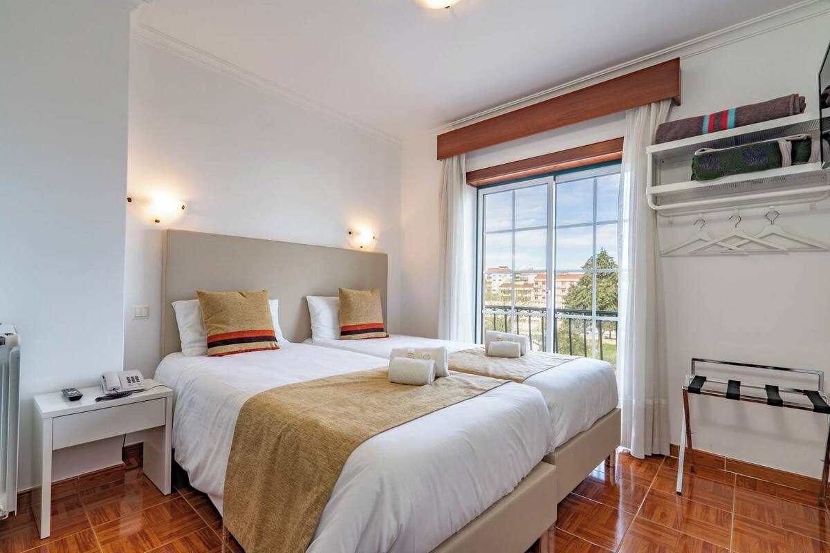Quarto de hotel com uma cama grande, mesas de cabeceira, um guarda-roupa e uma janela com vista.