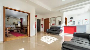 Un hall d’entrée spacieux avec un comptoir d’accueil, un canapé en cuir noir et un mur d’accent rouge.