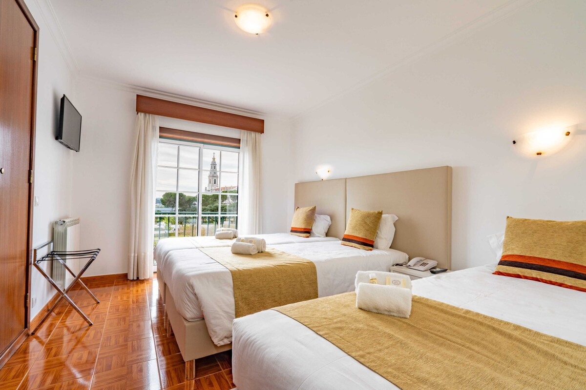 Een hotelkamer met twee bedden, een televisie, een raam met uitzicht op een gebouw en een verwarming.