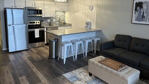 Une cuisine compacte équipée d’un réfrigérateur, d’une cuisinière et d’un évier, un coin repas avec des tabourets et un salon avec un canapé.