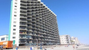 Un hôtel de grande hauteur doté de nombreux balcons, un ciel dégagé et une plage en arrière-plan.