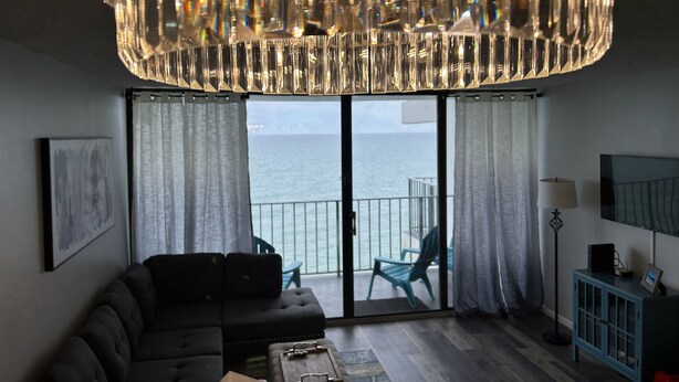 Un salon avec une grande fenêtre, un canapé de couleur sombre, une petite table et un meuble bleu.