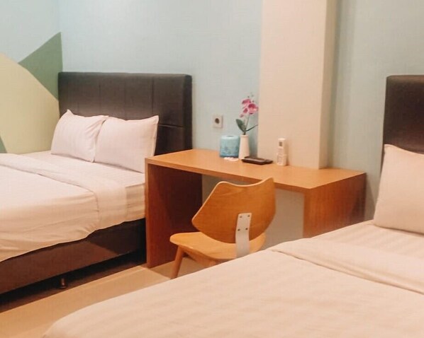 A hotel room with two beds, a wooden nightstand, a chair, and a small table with a vase of flowers. - Capital Hotel (Tangerang)