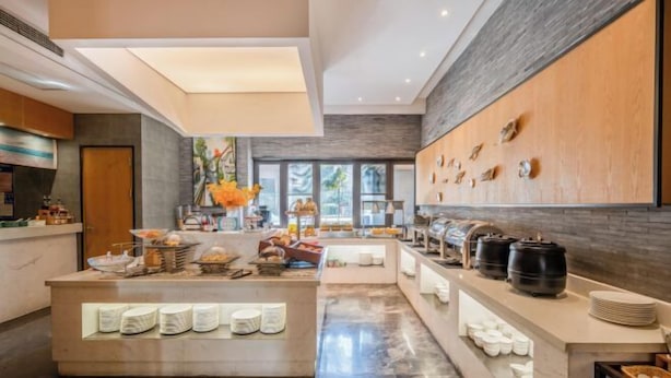 Un hall d’hôtel moderne doté d’un espace buffet central, d’un comptoir d’accueil et d’une grande fenêtre laissant entrer la lumière naturelle.